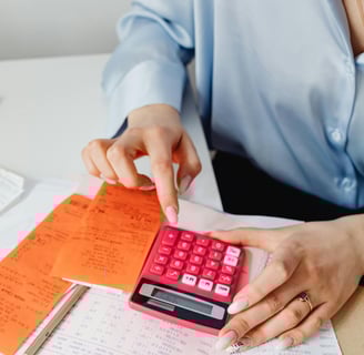 Person using a pink calculator while organizing receipts and documents on a desk.