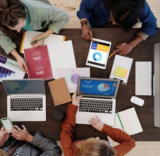 a group of people sitting around a table with laptops