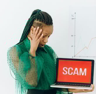 Woman in a green blouse holding a laptop displaying 'SCAM' while looking frustrated.