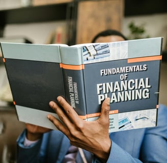 Person in a suit reading 'Fundamentals of Financial Planning' book with bookshelves in the background.
