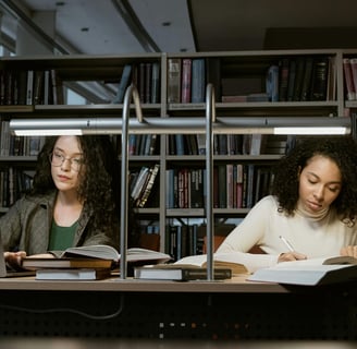 two women sitting at a table with books and a laptop