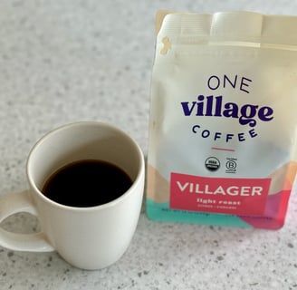 A cup of black coffee in a white cup sitting next to a bag of coffee beans