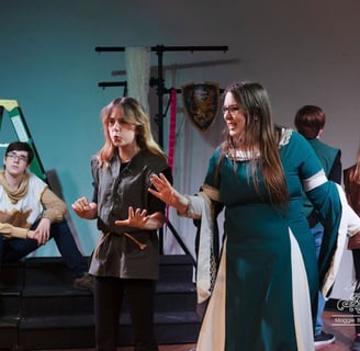 a teen actor playing Guinevere in Camelot in a green dress standing in front of a stage