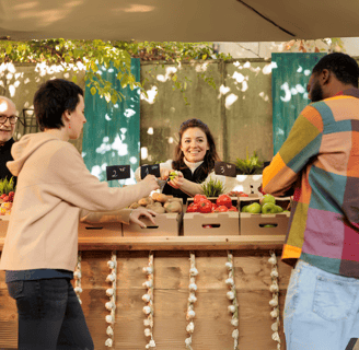 Customers buying fresh produce from a friendly vendor at a farmers' market, supporting local farmers