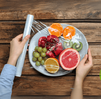 Hands wrapping fresh fruit on a plate with plant-based, eco-friendly food wrap over a rustic wooden