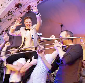 Groom lifted by friends on the dance floor while band plays live trombone