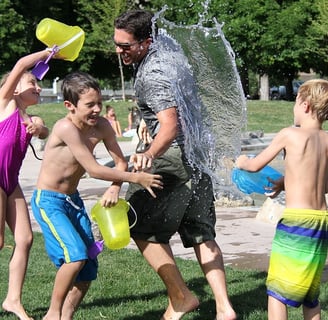 Parent and 3 children having a water fight in the garden on a sunny day