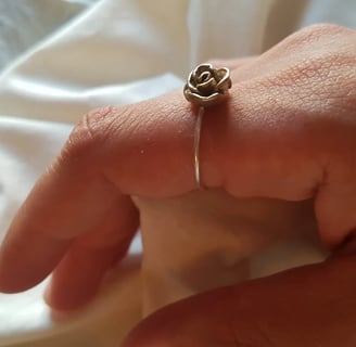 a person's hand holding a ring with a rose on it