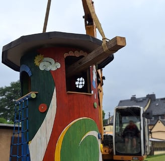 der bunte Spielturm aus Holz wird an Schleppen zum Standort gehoben