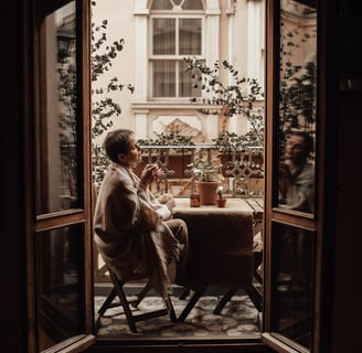 Woman wrapped in a blanket sitting at a cozy outdoor table with tea, enjoying a quiet moment.