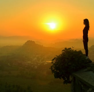 Silhouette of a woman standing calmly on a ledge overlooking a sunrise-lit valley, symbolizing peace