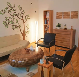 Innenansicht der Praxis: Ein gemütliches Sofa, zwei gemütliche Sessel und Holzmöbel