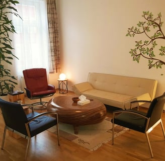 Innenansicht der Praxis: Ein gemütliches Sofa, drei gemütliche Sessel und ein Holztisch