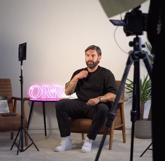 a man sitting in a chair with a pink neon sign
