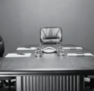 grayscale image of an empty conference room, one chair at the head of the table