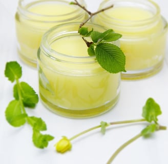 Potes de creme natural amarelo com folhas verdes e flores decorativas, representando cosméticos artesanais à base de ingredie