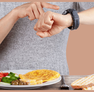 Pessoa olhando para o relógio enquanto se prepara para uma refeição com legumes e pão, representando o jejum intermitente.