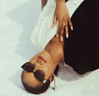 a woman in a white shirt and sunglasses laying on a bed