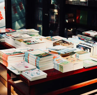 A selection of piles of books upon a table in what appears to be a bookshop.