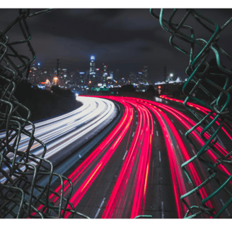 View of freeway at night through broken chainlink fence