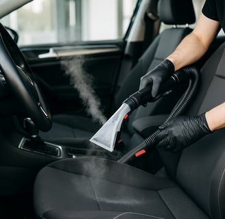: Detailing technician using steam cleaner to sanitize and deep clean car seats.