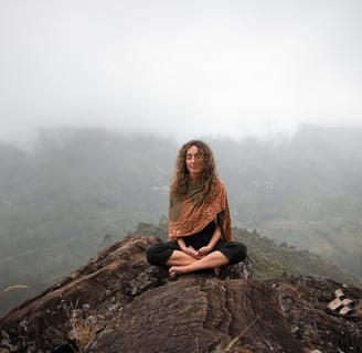 Woman meditating on a mountain top with misty hills in the background