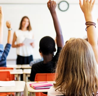 An image of a classroom with a teacher and students learning and raising their hands with curiosity