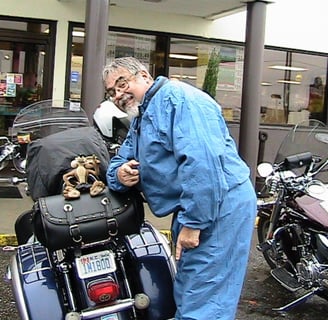 Biker pauses for a picture of a motorcycle and a toy on the back seat.