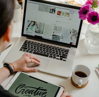 Woman looking at laptop for hand-signed calligraphy designs for the logo she is creating on her iPad that say Creative
