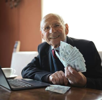 Um homem rico e idoso mexendo no laptop e segurando muito dinheiro.