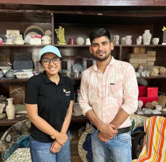 Team member and artisan standing in front of a shelf of gaurahari products.