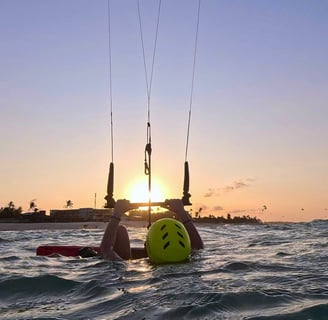 mulher dentro da água segurando o kite e vendo o por do sol.