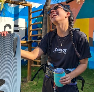 mulher jovem, sorrindo segurando um copo e uma prancha de kitesurf