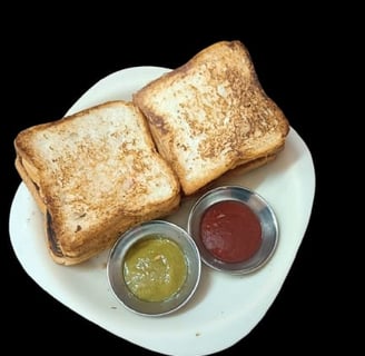 alt="Toasted Veg Sandwich served with spicy green chutney and sweet red sauce on a white plate"