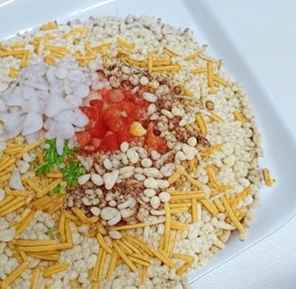 alt="Bengali Jhalmuri served on a plate, made with puffed rice, chopped onions, tomatoes, green chil