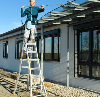 Auf einer Leiter wird mit einer Fensterputzerverlängerung ein Vordach gereinigt. 