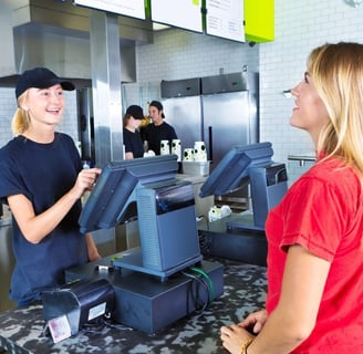 A customer orders off of a menu while the worker takes her order on a point of sale machine.