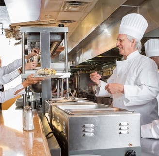 A chef hands a finished dish to a waitress in the kitchen of a restaurant.