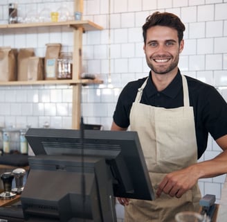 A happy store owner works at his coffee shop's point of sale system.