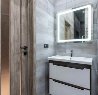 Photo of a modern bathroom vanity with illuminated mirror and grey tiled