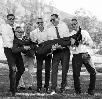 Photo en noir et blanc d'un marié porté par ses amis lors d'une séance de photos de groupe.