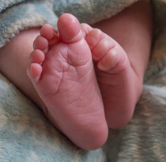 Close-up of a baby's toes peeking out from a soft blue blanket, with one foot's toes gently curled inward.