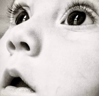 Black and white close-up of a baby girl's face, looking upward with wide eyes, capturing a sense of wonder and innocence