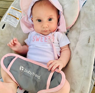 A newborn baby girl with a pink sunhat sitting in a bouncer, looking at the camera