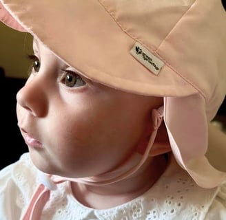 close-up profile of a baby wearing pink bucket hat, sunlight shining in her eyes and illuminating her face with a warm glow