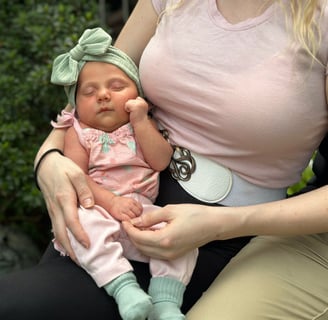 A mother in a pink shirt holding her sleeping baby in a green bow resting with hand on cheek.