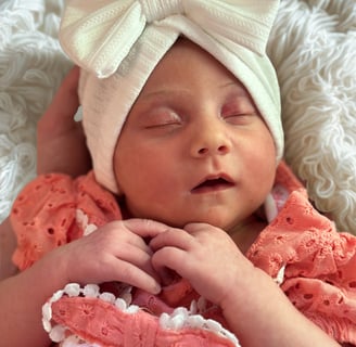 A peaceful newborn sleeping on a fluffy white blanket wearing a wink shirt and a white bow