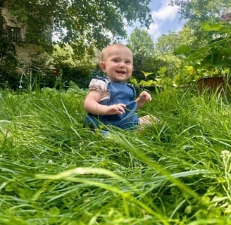 A happy baby girl sitting in the tall grace smiling at the camera representing mother baby bond