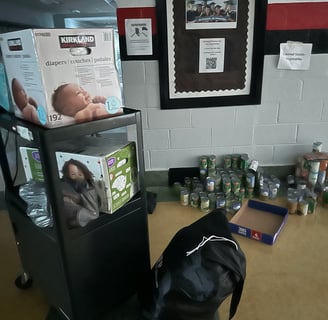 A dark middle school hall food pantry with cans of food and baby supplies during Hurricane Helene
