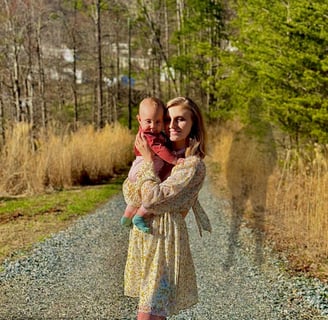 A mother holding baby on a gravel road at dusk, with the shadow of the father looming behind—tension of co-parenting & abuse 